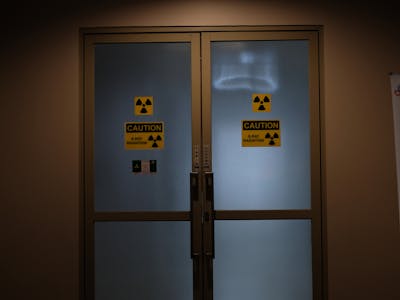 Closed doors of a radiology department room with caution signs for radiation warning, dimly lit indoor scene.