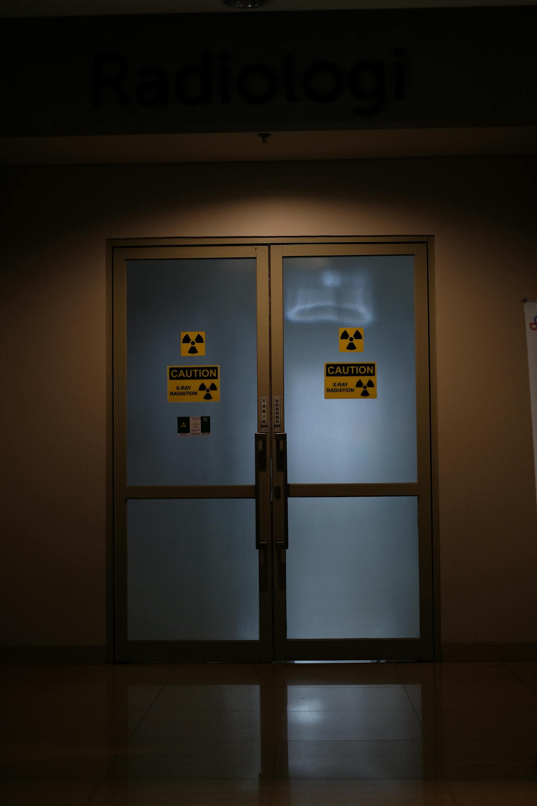 Closed doors of a radiology department room with caution signs for radiation warning, dimly lit indoor scene.